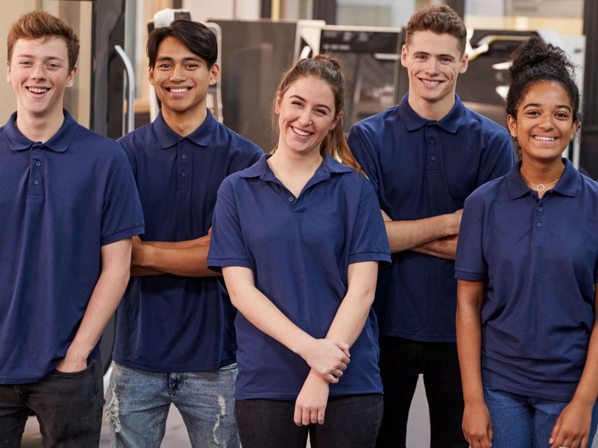 Eine Gruppe von Auszubildenden steht in einer Fabrik und schaut lächelnd in die Kamera