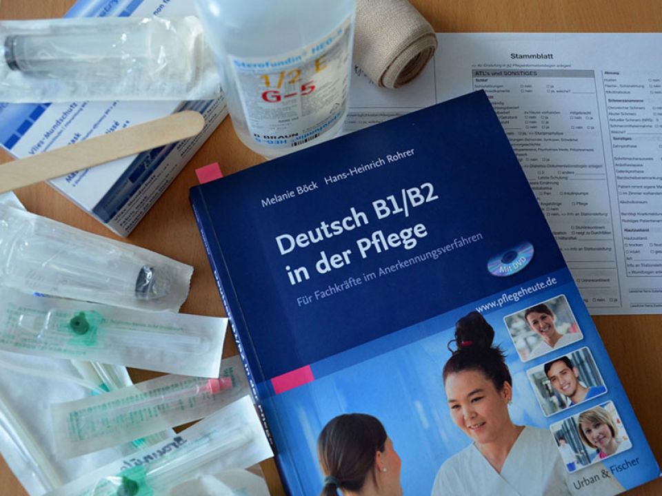 Lehrbuchbuch Deutsch B1/B2 in der Pflege mit Utensilien, die in der Pflege benötigt werden