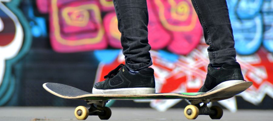 Eine jugendliche Person fährt auf einem Skateboard, im Hintergrund sind an einer Wand bunte Grafittis