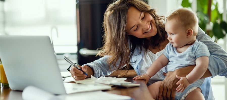 Eine junge Mutter arbeitet am Schreibtisch und hat dabei ihr Baby auf dem Schoß