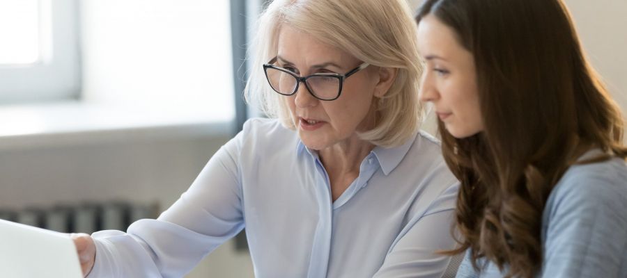 Eine ältere Frau sitzt mit einer jüngeren Frau am Laptop und coacht sie