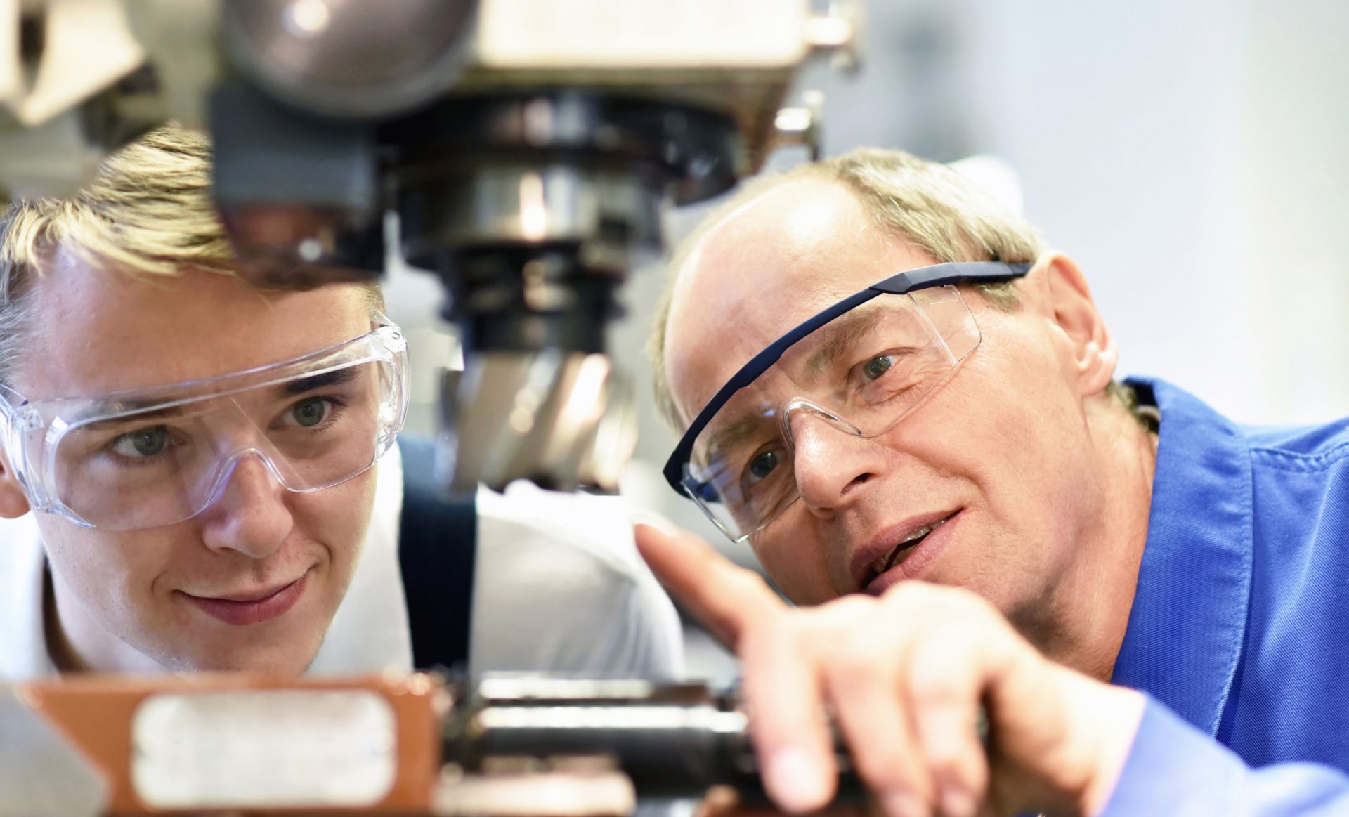 Ein Auszubildender und sein Meister schauen auf eine Maschine, die der Meister dem Auszubildenden erklärt
