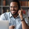 Ein people of colour-Mann sitzt an einem Laptop und trägt ein Headset, um an einem Webinar teilzunehmen.