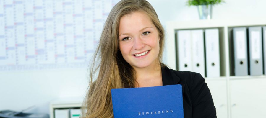 Junge Frau hält Bewerbungsunterlagen in Händen und lächelt in die Kamera
